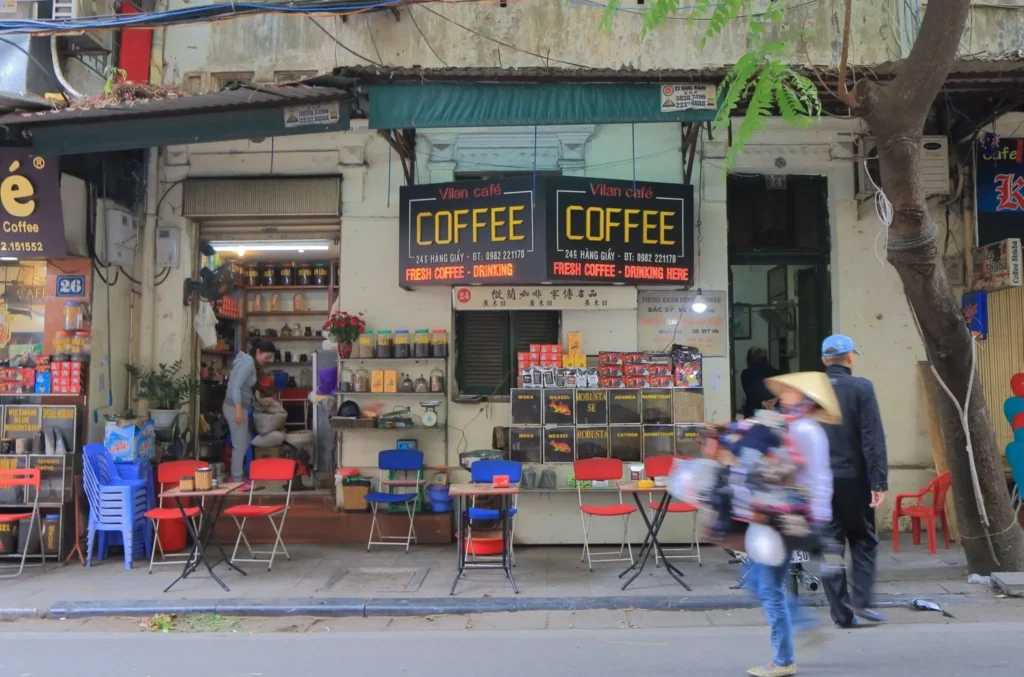 A female solo traveler with brown hair sitting at a tiny sidewalk cafe table in the Hanoi Old Quarter enjoying a traditional Vietnamese egg coffee.