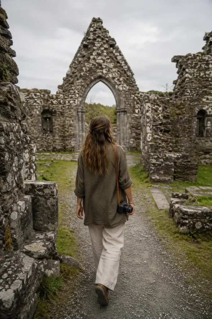 A solo woman traveler explores the historic stone ruins of an ancient abbey during a road trip through rural Ireland.