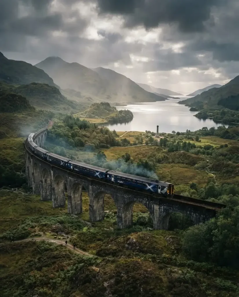 ScotRail train crossing the Glenfinnan Viaduct with sea and islands beyond on the West Highland Line to Mallaig, Scotland